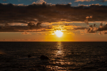 Watching the sunset at the port of Puerto de la Cruz, Tenerife, Canary Islands, Spain, Europe. View of the horizon of Atlantic Ocean. The sun is reflecting in the calm sea. Vibrant clouds in the sky