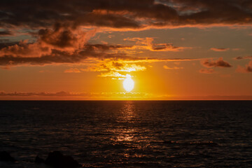 Watching the sunset at the port of Puerto de la Cruz, Tenerife, Canary Islands, Spain, Europe. View of the horizon of Atlantic Ocean. The sun is reflecting in the calm sea. Vibrant clouds in the sky