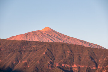 Panoramic view on the peak of volcano Pico del Teide during sunrise seen from the port of Puerto de la Cruz, Tenerife, Canary Islands, Spain, Europe. The summit turns vibrant red during golden hour