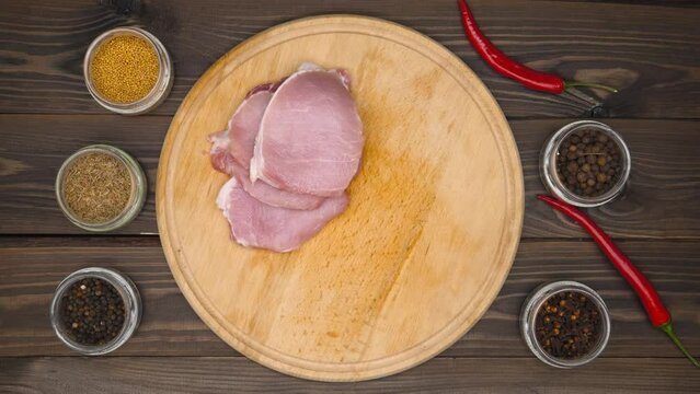 Hands put meat on the board. The chef lays out pink beef steaks on a wooden cutting board. Pork meat is being prepared for marinating. Spices, red hot chili peppers, Cumin, mustard. Close-up. Top view
