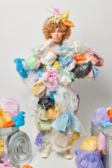 Vertical shot of displeased irritated woman picked plastic litter considers pollution problem collects wastes tries to distract from environmental problems isolated over grey background. Planet saving