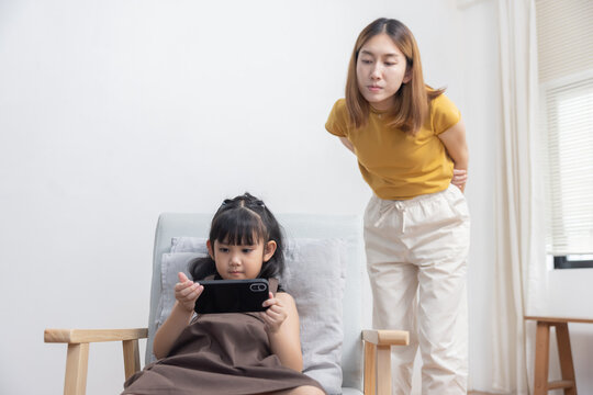 Upset Asian Mother Looking at Her Kid Playing Game on the Smartphone