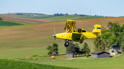 Yellow Crop Duster flies over a farm house and fields