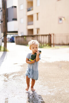 Little girl walks barefoot in a puddle, clutching her shoes to her chest. High quality photo