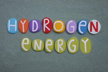 Hydrogen Energy, creative text composed with multi colored stone letters over green sand