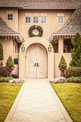 Sidewalk leading to Arched door to upscale modern stucco home with Christmas wreath and electric icicles