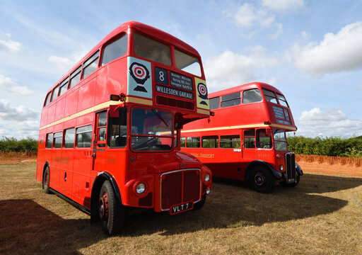 Two Vintage Red Double Decker Buses parked on grass.