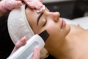 Facial cleansing with ultrasound scrubber. Woman receiving ultrasound facial peeling and cleansing....