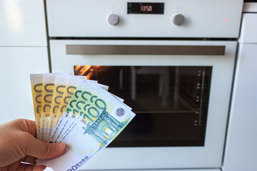 Man is holding money in his hands near the electric oven. Increase in the price of electricity....