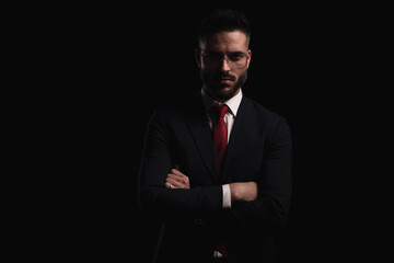 elegant young bearded man in black suit with red tie folding arms