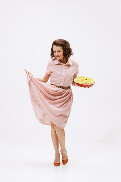 Portrait of beautiful woman in stylish pink dress, holding apple pie isolated over white background