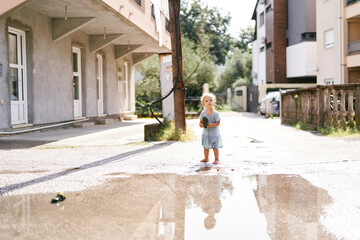 Fototapeta na wymiar Little girl stands barefoot in a puddle holding a sandal in her hands. High quality photo