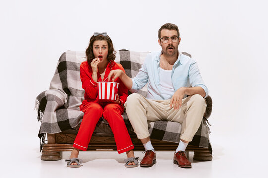 Portrait of couple, man and woman watching TV, movie together with interest isolated on white background. Eating popcorn