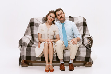 Portrait of beautiful couple, man and woman sitting on sofa and looking at camera isolated over white background