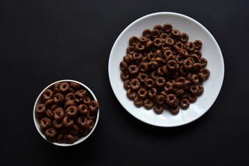 Breakfast of chocolate and honey cornflakes on white plates on a black background. Delicious breakfast of cornflakes close-up.