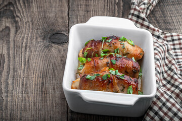 Chicken breasts wrapped in bacon in white dish on wooden table