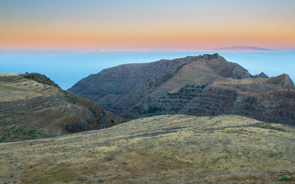 Sunrise over a landscape with mountains and deeply incised valley on the northwest coast of the isle of La Gomera with the isle of La Palma in the background, Spain