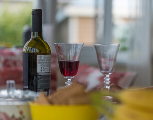 a bottle of red wine and a poured glass against the background of a set table and bright windows