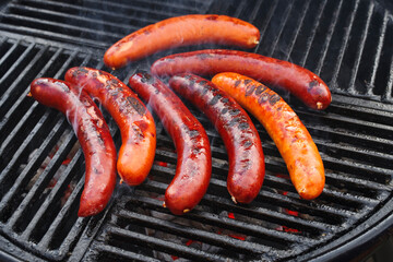 Traditionelle deutsche Bratwurst vom Grill angeboten als close-up auf einem Holzkohlegrill mit Feuer und Rauch 