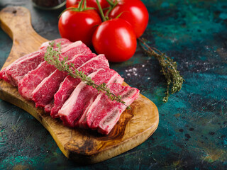 On a dark green marble background, raw meat steaks with a sprig of rosemary on a cutting board and red fresh tomatoes. Delicious organic food, healthy lifestyle. Home kitchen.