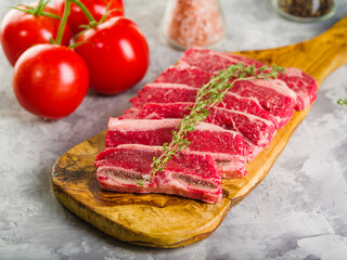 Meat steaks with a sprig of rosemary on a wooden cutting board are waiting to be cooked. Ripe tomatoes, spices on a light background. Home kitchen. Recipes for meat dishes.