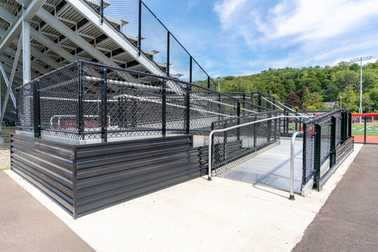 Accessible wheelchair ramp with railings and slip resistant surface at empty metal stadium bleacher.  Nondescript location with no people in image.  Not a ticketed event.  	