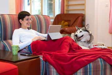 Young woman drinking coffee and using laptop and smartphone while sitting on the sofa at home with...