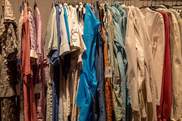 Row of colourful tone fabric and stylish shirts hang on aluminium hanger clothes rack for fitting in retail fashion store or second hand outlet shop.