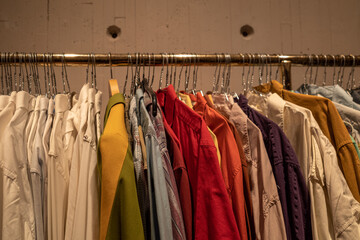 Row of colourful tone fabric and stylish shirts hang on aluminium hanger clothes rack for fitting...