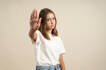 Young brunette woman in a t-shirt over isolated beige background stopping singing with her palm....