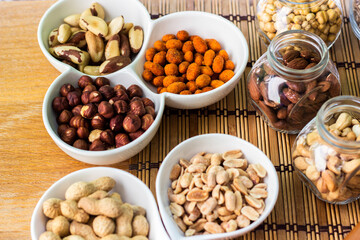 Rustic wood table filled with a large assortment of nuts like pistachios, hazelnut, pine nut, almonds, pumpkin seeds, sunflower seeds, peanuts, cashew and walnuts