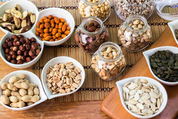 Rustic wood table filled with a large assortment of nuts like pistachios, hazelnut, pine nut, almonds, pumpkin seeds, sunflower seeds, peanuts, cashew and walnuts
