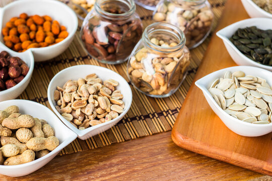 Rustic wood table filled with a large assortment of nuts like pistachios, hazelnut, pine nut, almonds, pumpkin seeds, sunflower seeds, peanuts, cashew and walnuts