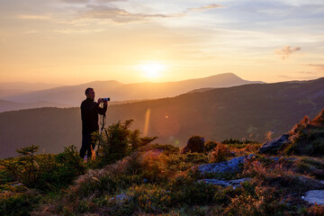 Photographer with the tripod takes photos of the mountains at the sunset.
