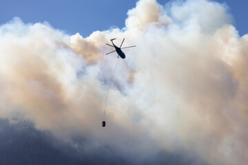 Wildfire Service Helicopter flying over BC Forest Fire and Smoke on the mountain near Hope during a hot sunny summer day. British Columbia, Canada. Natural Disaster