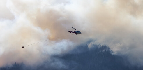 Wildfire Service Helicopter flying over BC Forest Fire and Smoke on the mountain near Hope during a hot sunny summer day. British Columbia, Canada. Natural Disaster