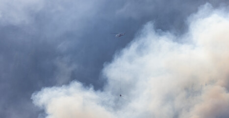 Wildfire Service Helicopter flying over BC Forest Fire and Smoke on the mountain near Hope during a hot sunny summer day. British Columbia, Canada. Natural Disaster