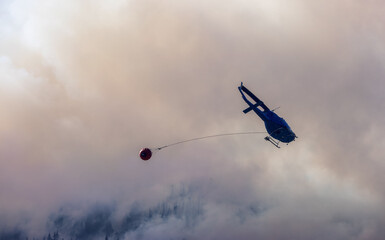 Wildfire Service Helicopter flying over BC Forest Fire and Smoke on the mountain near Hope during a hot sunny summer day. British Columbia, Canada. Natural Disaster