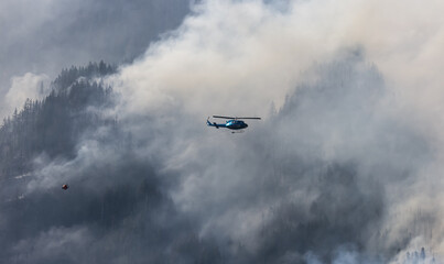 Wildfire Service Helicopter flying over BC Forest Fire and Smoke on the mountain near Hope during a hot sunny summer day. British Columbia, Canada. Natural Disaster