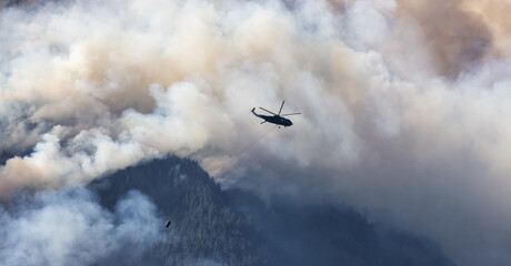 Fototapeta premium Wildfire Service Helicopter flying over BC Forest Fire and Smoke on the mountain near Hope during a hot sunny summer day. British Columbia, Canada. Natural Disaster
