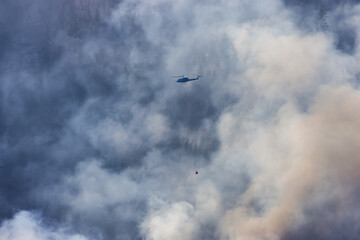 Wildfire Service Helicopter flying over BC Forest Fire and Smoke on the mountain near Hope during a hot sunny summer day. British Columbia, Canada. Natural Disaster