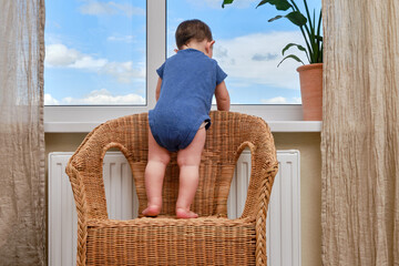 Toddler baby climbs to the window on the windowsill. Child crawls to the window holding on to the...