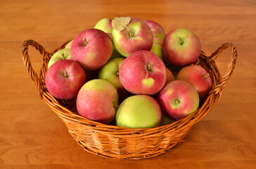 Close-up of fresh red and green apples in a wicker basket on a wooden table.