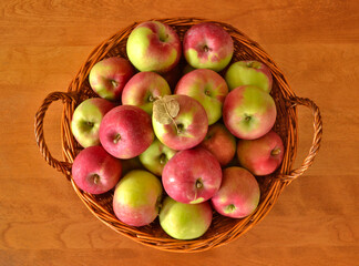 Top view of fresh red and green apples in a wicker basket on a wooden table.
