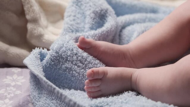 Infant baby feet on a bed. Close up of toddler's bare feet. Cute little baby feets lying on bed. Baby feet on blue blanket. Toddler is moving delicate, gentle his little fingers. 
