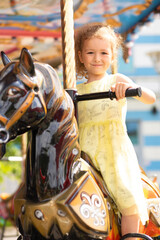 Obraz na płótnie Canvas Adorable little toddler girl on carousel horse. child on attraction. kid entertainment. Happy healthy baby having fun outdoor on sunny day. Family weekend, vacations, holiday. vertical
