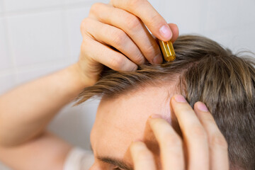 Middle aged caucasian white man uses, applies to hair with cosmetic ampoules with serum for hair growth, restoration beauty hair. The concept of the problem of male hair loss, baldness and alopecia