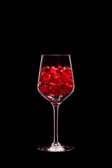 Wine glass filled with transparent red heart shape crystals backlit and isolated on black background. Love and celebration concept. Copy space.