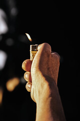 man hand holding lighter with flame on dark background, toned image