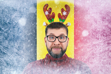 portrait bearded young man in funny Christmas reindeer horns and glasses positive smile on background frozen of belgium flag, holidays and Christmas vacations, gas crisis in EU countries